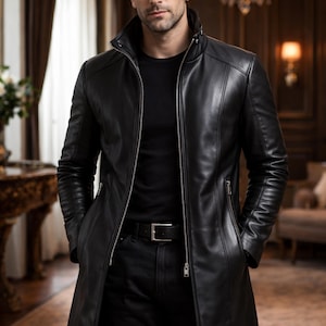May include: A black leather jacket with a zip-up front and a high collar. The jacket is long, reaching to the mid-thigh, and is worn with a black shirt and black pants. The image is set in a room with a chandelier.