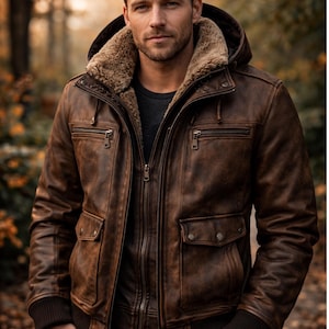 May include: A brown leather jacket featuring a detachable hood with a tan faux fur lining, a full-length front zipper, two chest pockets with zippers, two lower flap pockets with snap buttons, and dark brown ribbed cuffs at the sleeves and waist.