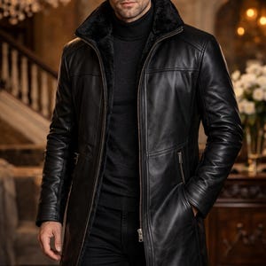 Könnte beinhalten: Schwarzer Ledermantel mit Kunstfellkragen und Reißverschluss. Der Mantel hat eine lange Länge und eine taillierte Passform. Das Model trägt einen schwarzen Rollkragenpullover und eine schwarze Hose. Ein stilvolles Oberbekleidungsstück.