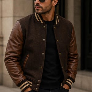 May include: A brown wool varsity jacket with brown leather sleeves. The jacket has a button-up front, striped cuffs, and a striped collar. The brand logo "PLANIO" is visible in the upper left corner.