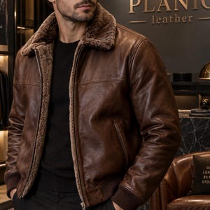 May include: A brown leather jacket featuring a plush, textured brown faux fur collar and interior lining. The jacket includes a front metal zip closure, long sleeves with ribbed brown cuffs, and two side pockets. The text PLANIC leather is visible.