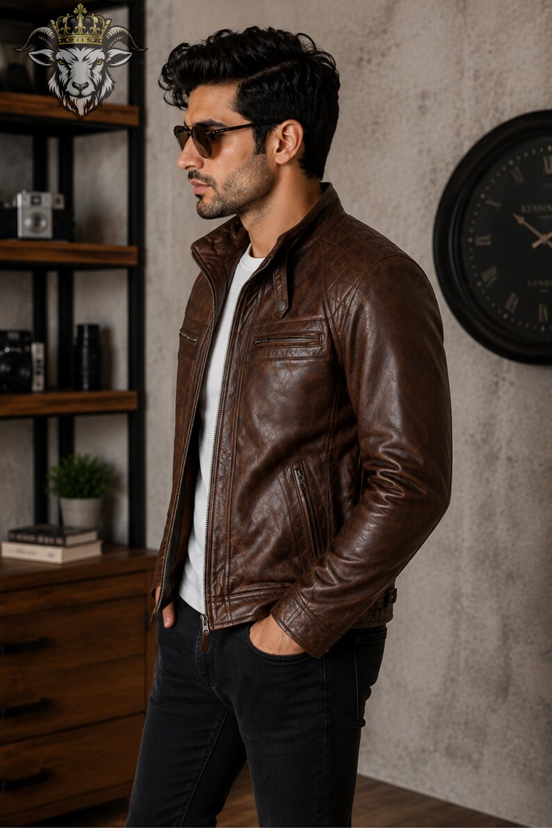 May include: A brown leather jacket featuring a stand-up collar, a front zipper closure, and quilted shoulder detailing. The jacket includes two zippered chest pockets and two lower zippered pockets, worn over a plain white t-shirt and black jeans.