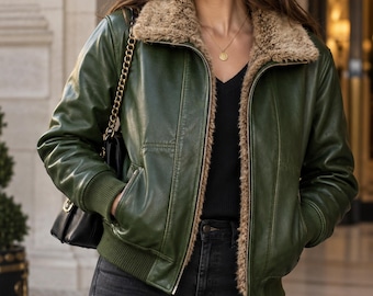 May include: A forest green bomber jacket featuring a tan faux fur collar and lining, a front metal zipper closure, ribbed cuffs and hem, and two side pockets. The jacket is worn over a black v-neck top and dark grey jeans with a black shoulder bag.