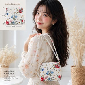 May include: A white wristlet bag featuring a colourful floral pattern with red, blue, and green flowers. The bag includes a wrist strap and measures 16 cm in height and 18 cm in width as indicated by the text and diagram in the image.