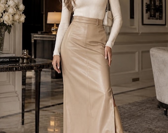 May include: A cream-colored ribbed turtleneck long-sleeve top paired with a high-waisted beige faux leather maxi skirt featuring a side slit and a matching belt. The outfit is completed with beige pointed-toe knee-high boots and a small shoulder bag.
