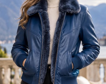May include: A blue leather bomber jacket featuring a dark blue faux fur collar and interior lining, a front zipper closure, ribbed cuffs and hem, worn over a cream-colored turtleneck sweater and black pants.