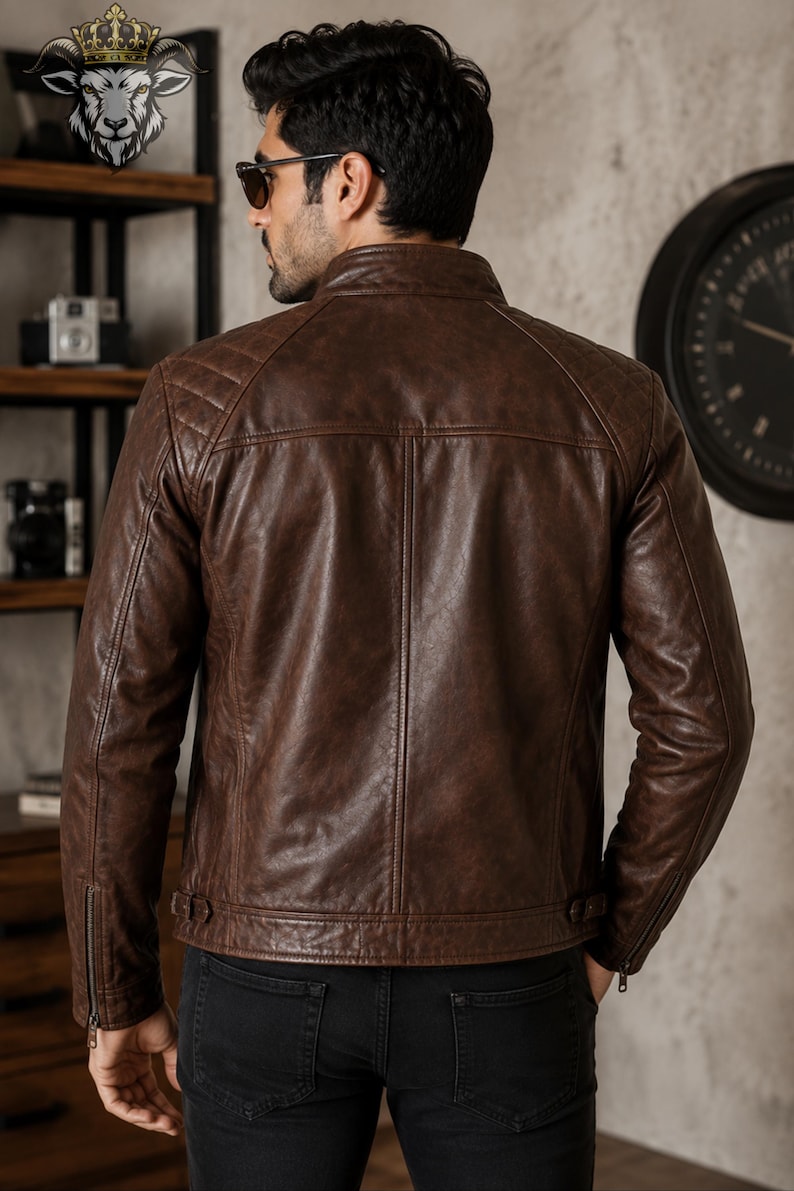 May include: A brown leather jacket featuring a stand-up collar, quilted shoulder panels, and long sleeves with zippered cuffs. The back of the jacket displays vertical seam detailing and adjustable side tabs at the hem, worn over black trousers.