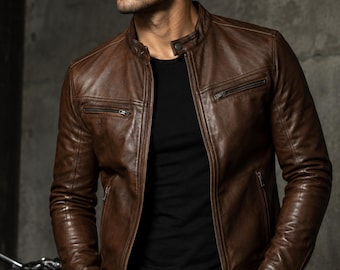 May include: A brown leather jacket featuring a mandarin collar with a snap button closure, a full-length front zipper, and two horizontal zippered chest pockets. The jacket has long sleeves with zippered cuffs and is worn over a black t-shirt.