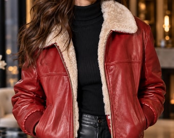 May include: A red leather jacket featuring a beige faux fur collar and lining, a front zipper closure, and ribbed knit cuffs. The jacket is worn over a black ribbed turtleneck sweater and black pants, showcasing a classic design with side pockets.