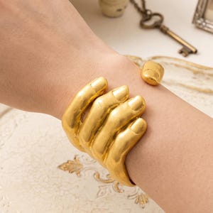 Skulpturalt guldfärgat handmanschettarmband, Schiaparelli-stil, surrealistiska statementsmycken