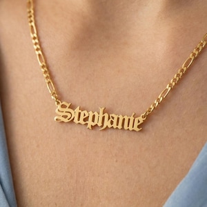 May include: A gold-colored necklace with the name "Stephanie" in an elegant script font. The necklace has a delicate chain and is displayed against a light blue background.