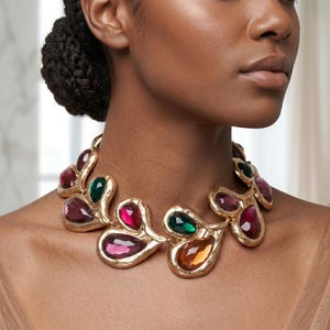 May include: A gold-coloured statement necklace with large, colourful gemstone pendants in shades of red, green, and orange. The necklace has a textured, organic design, and the gemstones are teardrop-shaped.