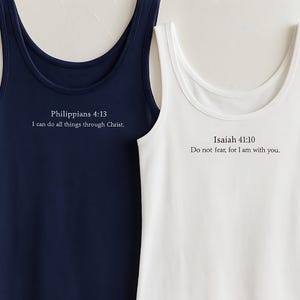 May include: Two sleeveless tank tops, one navy blue and one white. The navy top has the text "Philippians 4:13 I can do all things through Christ." The white top has the text "Isaiah 41:10 Do not fear, for I am with you."