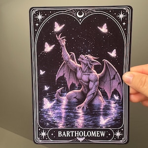 May include: A rectangular print featuring a stone-textured gargoyle creature kneeling in dark water, reaching toward glowing butterflies under a starry night sky with a crescent moon. The bottom border displays the text BARTHOLOMEW in white.
