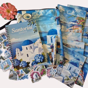 Puede incluir: Un conjunto de art&iacute;culos de papeler&iacute;a y accesorios con tem&aacute;tica de Santorini. Incluye un cuaderno de espiral, pegatinas, una bolsa con cremallera, postales, un bol&iacute;grafo y cinta decorativa. El cuaderno y las postales presentan im&aacute;genes de edificios blancos con c&uacute;pulas azules.