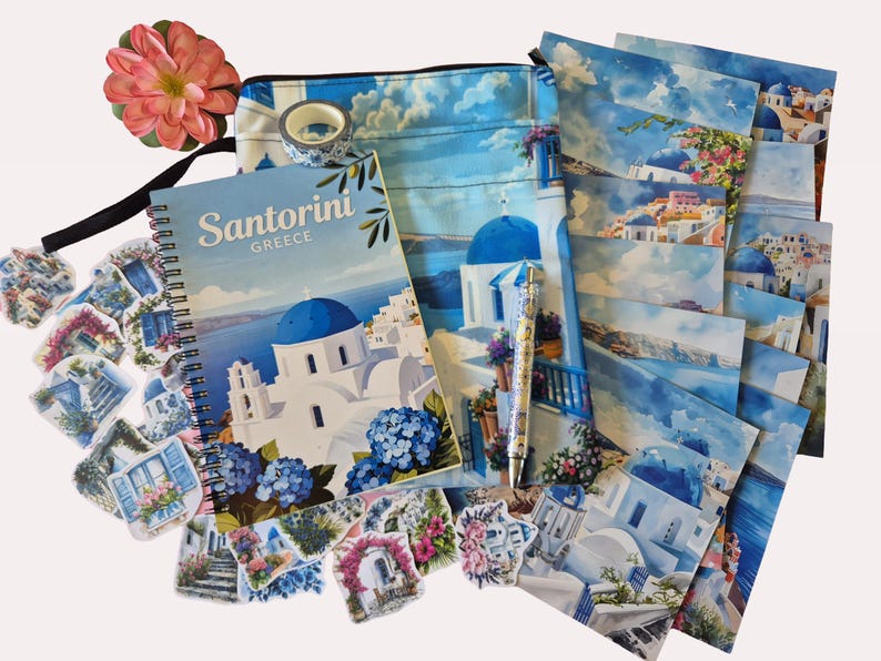 Puede incluir: Un conjunto de art&iacute;culos de papeler&iacute;a y accesorios con tem&aacute;tica de Santorini. Incluye un cuaderno de espiral, pegatinas, una bolsa con cremallera, postales, un bol&iacute;grafo y cinta decorativa. El cuaderno y las postales presentan im&aacute;genes de edificios blancos con c&uacute;pulas azules.