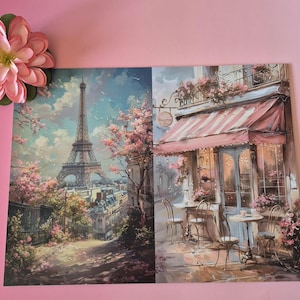 以下が含まれることがあります： パリの風景を描いた2つのアートプリント。1つは、ピンクの花咲く木々に囲まれたエッフェル塔を示しています。もう1つは、赤と白のストライプのオーニング、テーブル、椅子のあるカフェを描いています。ピンクの花が左上隅にあります。