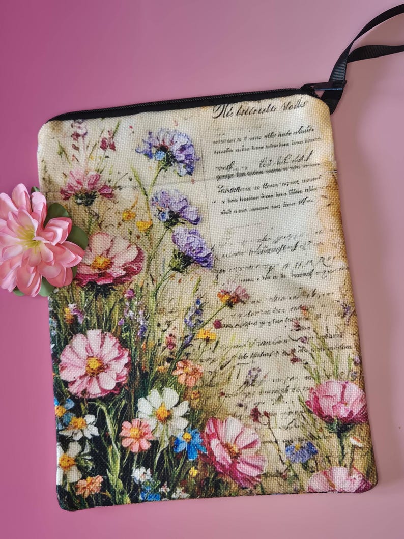 May include: A rectangular floral print pouch with a black zipper and strap. The pouch features a vintage-style design with pink, purple, and white flowers against a backdrop of handwritten script. The text "Nie bettreshe Molls" is visible.