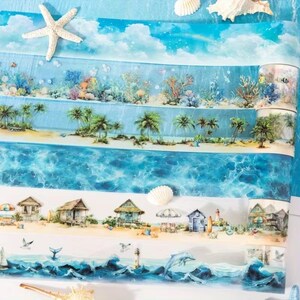 Op de afbeelding: Een rol decoratieve tape met meerdere horizontale stroken met kustthema's, waaronder een blauwe lucht met wolken, een onderwater koraalrif, een tropisch strand met palmbomen, oceaangolven, strandhuisjes en dolfijnen.