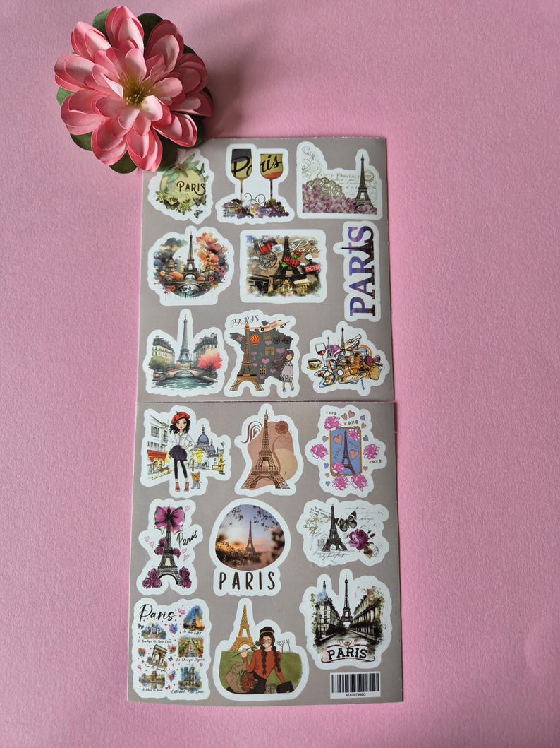 May include: Two sheets of Paris-themed stickers featuring the Eiffel Tower, wine glasses, and floral designs. The stickers are in various shapes and sizes, with the word "Paris" appearing on several. A pink flower is in the upper left corner.