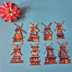 May include: A collection of paper windmills with detailed architectural designs, featuring brown, blue, and orange hues. A pink and red flower with a yellow center is positioned at the top left corner against a light blue background.