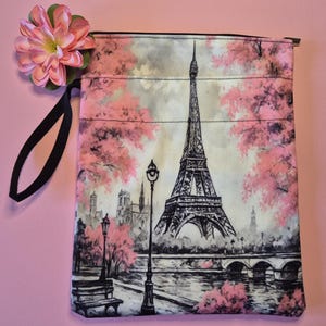Peut inclure: Une pochette rectangulaire en tissu avec une illustration en noir et blanc de la Tour Eiffel &agrave; Paris, en France, avec des fleurs de cerisier roses. La pochette a une poign&eacute;e noire et une fleur rose attach&eacute;e.