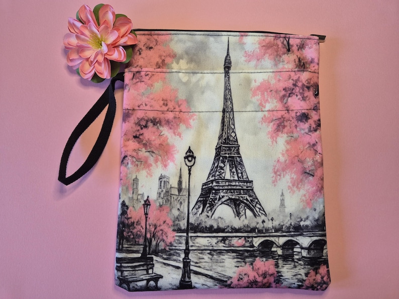 Peut inclure: Une pochette rectangulaire en tissu avec une illustration en noir et blanc de la Tour Eiffel &agrave; Paris, en France, avec des fleurs de cerisier roses. La pochette a une poign&eacute;e noire et une fleur rose attach&eacute;e.