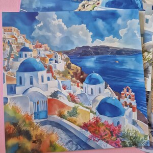 May include: Watercolour print depicting a Greek village with white buildings, blue domes, and the Aegean Sea. The artwork uses vibrant blues, reds, and oranges, with a cloudy sky. The print captures the essence of a coastal town.