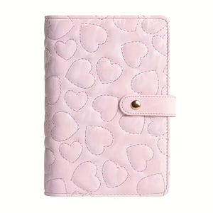 May include: A light pink, quilted planner with a heart pattern. The cover features stitched heart shapes and a matching strap with a gold snap closure. The planner is designed for organization and planning.