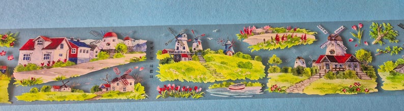 Op de afbeelding: Decoratieve washi tape met een aquarel landschap. Het toont huizen, windmolens en bloemen tegen een lichtblauwe achtergrond. De sc&egrave;ne omvat roodbedekte gebouwen en groene velden, die een dorp uitbeelden.