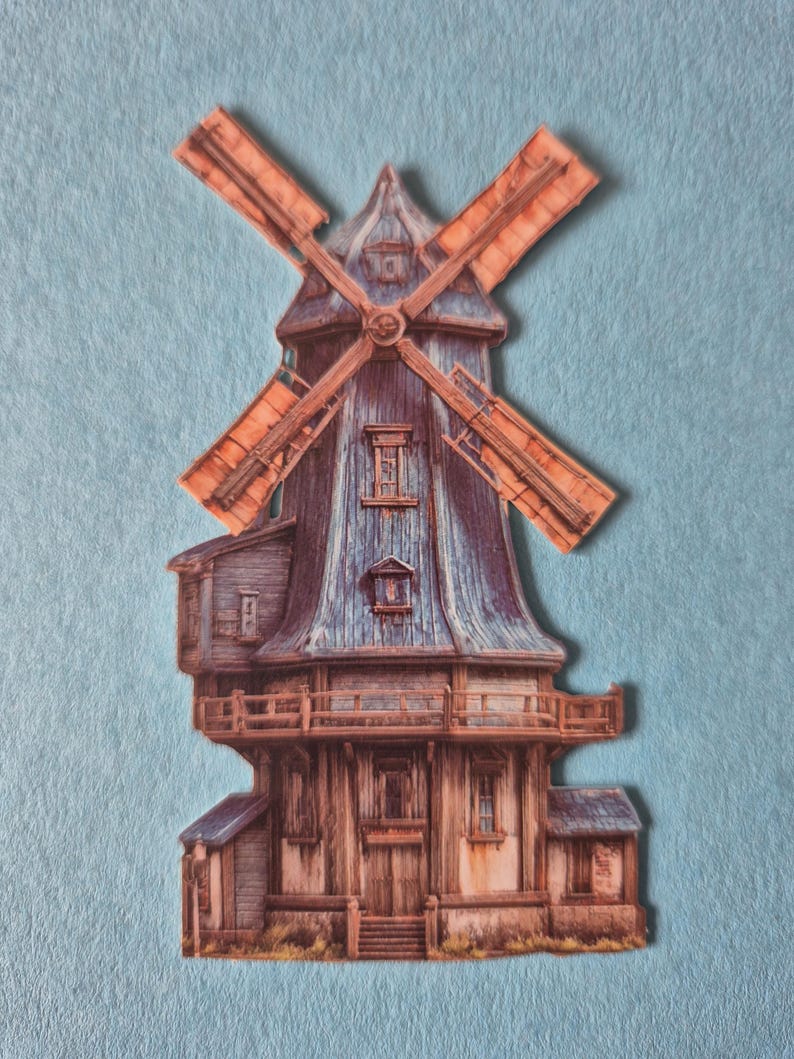 May include: A paper cutout of a windmill with a blue roof and orange blades. The windmill has a wooden exterior with multiple windows and a balcony. The background is a light blue felt.