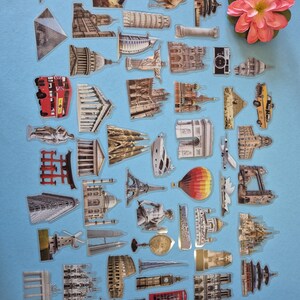 May include: A selection of clear stickers showcasing famous landmarks and travel themes. The stickers include images of the Eiffel Tower, the Statue of Liberty, and a red double-decker bus. A pink flower is also present, set against a blue backdrop.