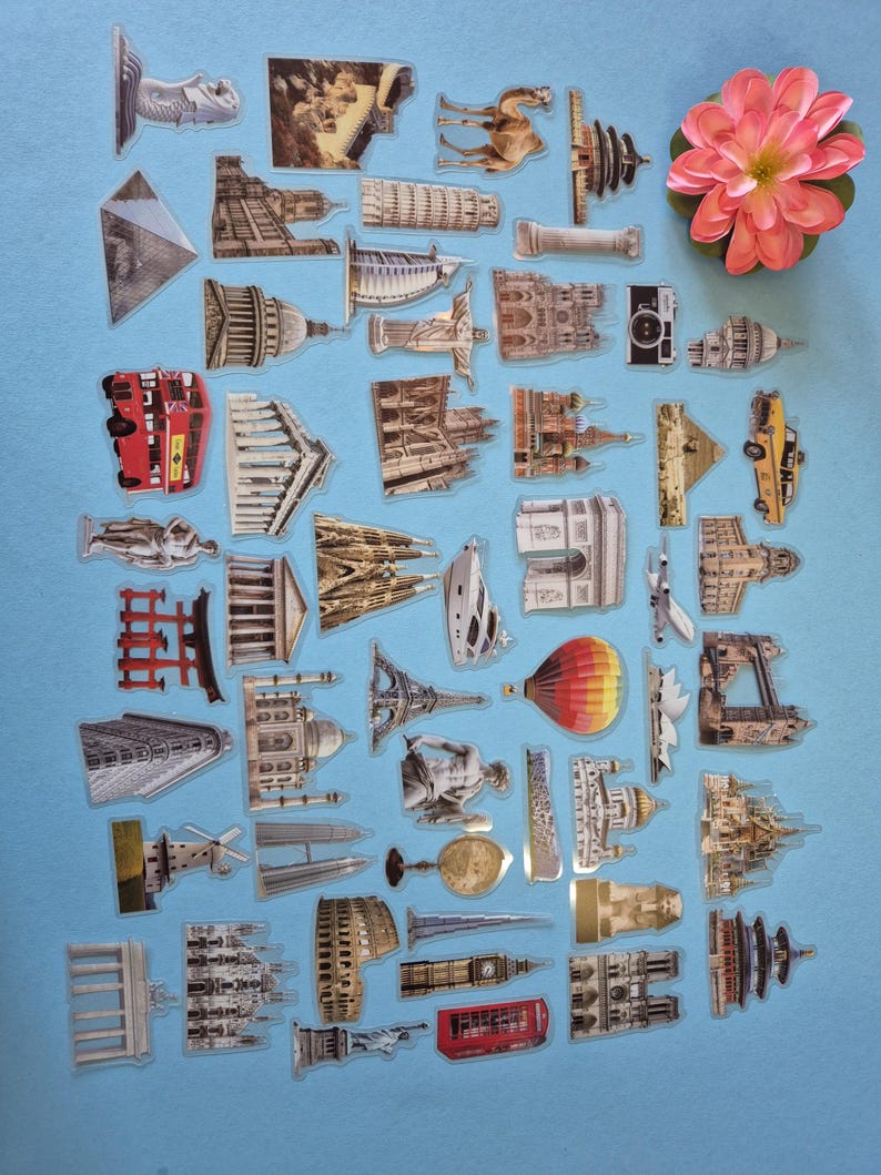 May include: A selection of clear stickers showcasing famous landmarks and travel themes. The stickers include images of the Eiffel Tower, the Statue of Liberty, and a red double-decker bus. A pink flower is also present, set against a blue backdrop.