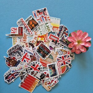 Peut inclure: Un assortiment d'autocollants sur le th&egrave;me de Londres, avec des motifs vari&eacute;s comme l'Union Jack, les cabines t&eacute;l&eacute;phoniques rouges et des paysages urbains. Les autocollants sont dispos&eacute;s sur un fond bleu clair, avec une fleur rose.