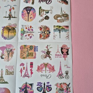 May include: Sheet of stickers featuring various designs with the Eiffel Tower, bicycles, and floral accents. The stickers include text such as "Paris," "Paris is my life," and "Paris France." The color palette includes pink, purple, and white.