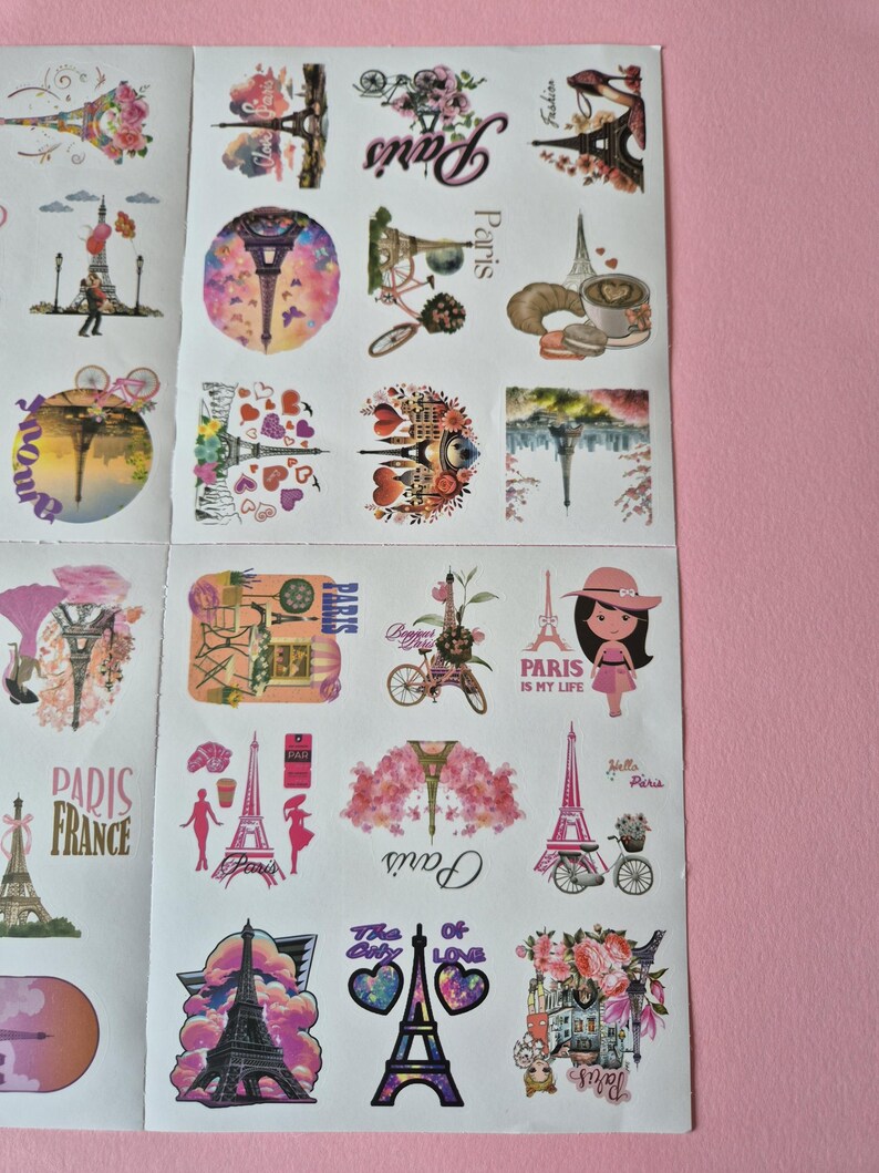 May include: Sheet of stickers featuring various designs with the Eiffel Tower, bicycles, and floral accents. The stickers include text such as "Paris," "Paris is my life," and "Paris France." The color palette includes pink, purple, and white.