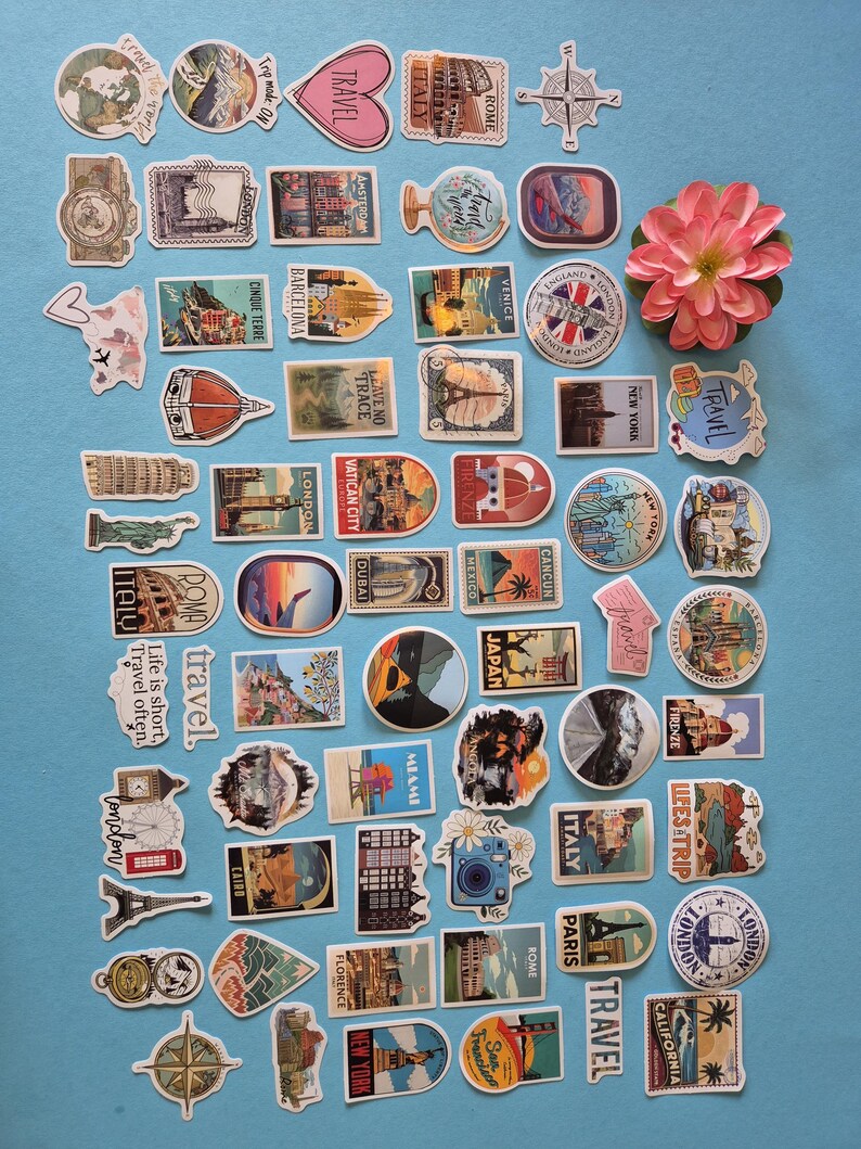 May include: A collection of travel-themed stickers featuring landmarks, compasses, and the word "travel." The stickers showcase various destinations like London, Paris, and Italy, with a pink flower in the upper right corner. The stickers are on a blue background.