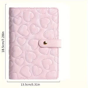 May include: A light pink journal with a quilted heart pattern. The journal measures 18.5 inches by 7.28 inches and 13.5 inches by 5.31 inches. It has a strap closure with a gold-colored snap.