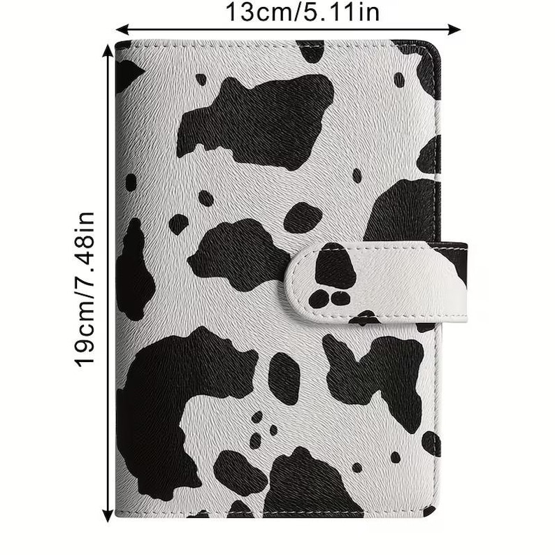 Op de afbeelding: Een planner met een koeienprint, 13 cm breed en 19 cm hoog. De omslag heeft een patroon van zwarte vlekken op een witte achtergrond. Het heeft een magnetische sluiting en een gestructureerd oppervlak.