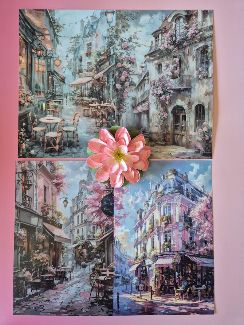 以下が含まれることがあります： カフェや花のアクセントがあるヨーロッパの街並みを描いた4つのアートプリント。大きなピンクの花がプリントの上に置かれています。プリントには、日よけ、テーブル、椅子のある建物が描かれており、ロマンチックな雰囲気を作り出しています。