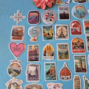 May include: A collection of travel-themed stickers featuring landmarks like the Eiffel Tower, the Statue of Liberty, and the Colosseum. The stickers are in various shapes and sizes, with a compass rose and a pink flower on a blue background.