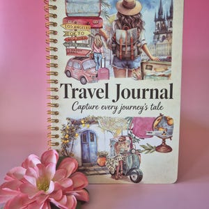 K&ouml;nnte beinhalten: Ein spiralgebundenes Reisetagebuch mit einer farbenfrohen Cover-Illustration. Das Cover zeigt eine Frau mit Rucksack, Koffern und einem Oldtimer. Der Text "Travel Journal" und "Capture every journey's tale" sind ebenfalls zu sehen.