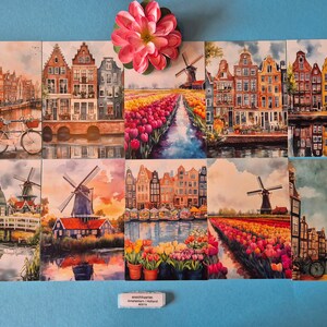 Op de afbeelding: Een verzameling aquarelprints met Nederlandse landschappen. De prints tonen grachten, windmolens en kleurrijke tulpenvelden. Een roze bloem ligt bovenop de prints. De tekst onderaan luidt "schoonbaarn Amsterdam / Holland 40/12".