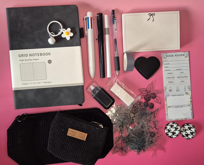 Puede incluir: Un set de papeler&iacute;a que incluye un cuaderno de cuadr&iacute;cula A5 gris oscuro con un llavero de flor, un bol&iacute;grafo multicolor, bol&iacute;grafos negro y blanco, un bloc de notas con lazo, un parche de coraz&oacute;n, una tarjeta de rese&ntilde;a de libros y sellos.