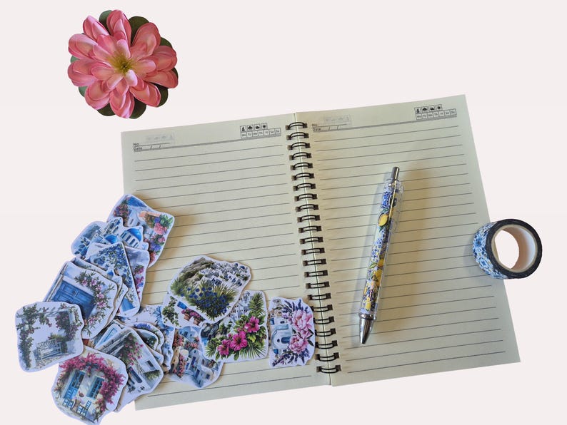 Puede incluir: Un cuaderno espiral abierto con p&aacute;ginas rayadas, un bol&iacute;grafo, pegatinas decorativas, un rollo de cinta washi y una flor rosa. El bol&iacute;grafo tiene un cuerpo transparente con un dise&ntilde;o floral. Las pegatinas representan escenas con flores y edificios.