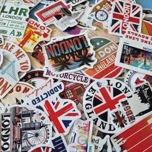 Peut inclure: Un assortiment d'autocollants sur le th&egrave;me de Londres, avec des drapeaux Union Jack, des monuments et des images de voyage. Les autocollants pr&eacute;sentent diverses couleurs et designs, avec des textes comme "London" et "England".