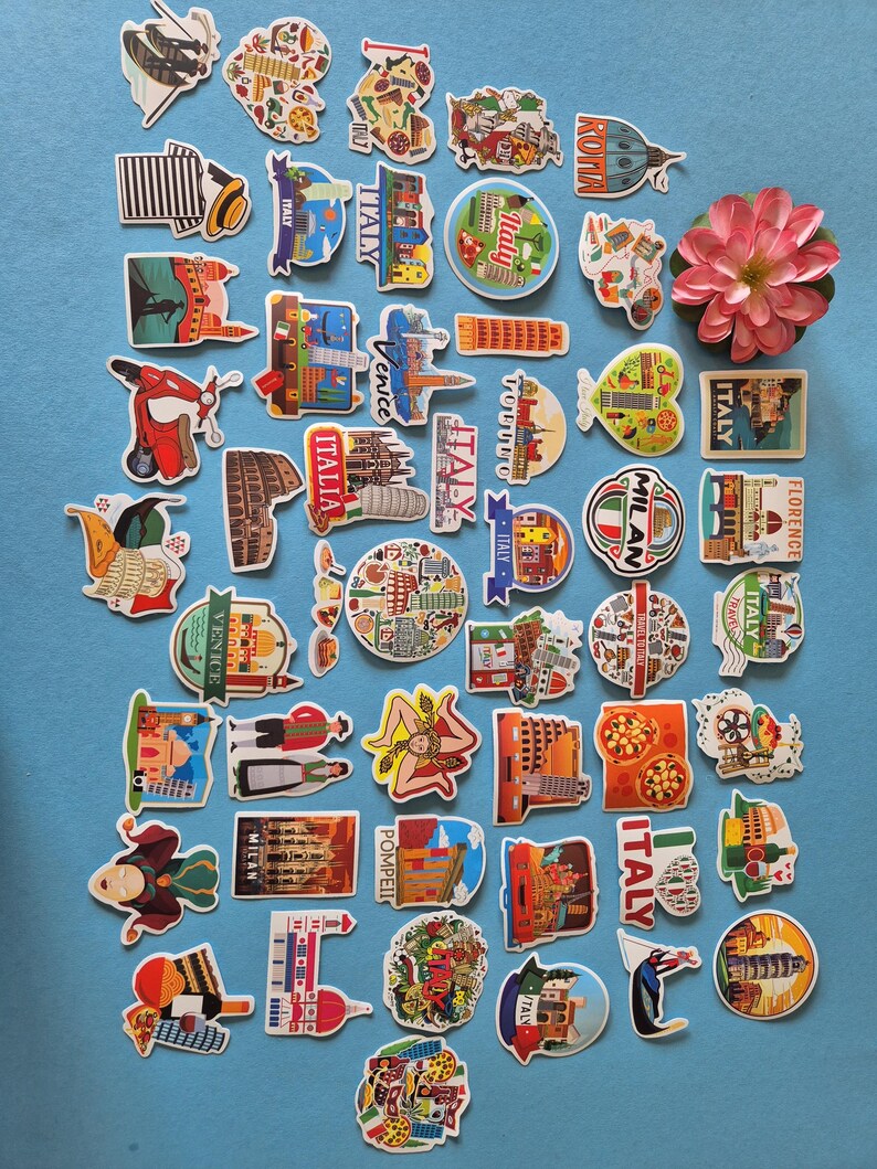 May include: A collection of colorful Italy-themed stickers and magnets, featuring iconic landmarks, food, and cultural symbols. Designs include the Leaning Tower of Pisa, pizza, and the Colosseum. A pink flower is also present.