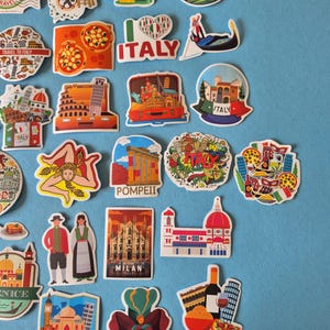 May include: A collection of colorful Italy-themed stickers featuring iconic landmarks, food, and cultural symbols. Designs include the Leaning Tower of Pisa, pizza, gondolas, and the Colosseum. The stickers are on a light blue background.