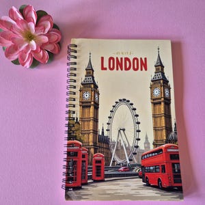 Op de afbeelding: Spiraalgebonden notitieboek met een Londen-ontwerp, met Big Ben, de London Eye en rode dubbeldekkerbussen. Het woord "LONDON" staat in het rood. Een roze bloem is linksboven te zien.