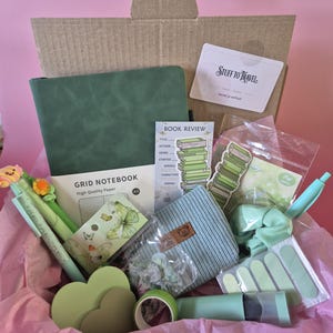 Pode incluir: Uma caixa de papel&atilde;o contendo um caderno de grade A5 verde, um cart&atilde;o de resenha de livro, uma pequena bolsa, um el&aacute;stico de cabelo verde, um rolo de fita verde, uma caneta verde com flores, tiras de unhas verdes e adesivos de borboletas.